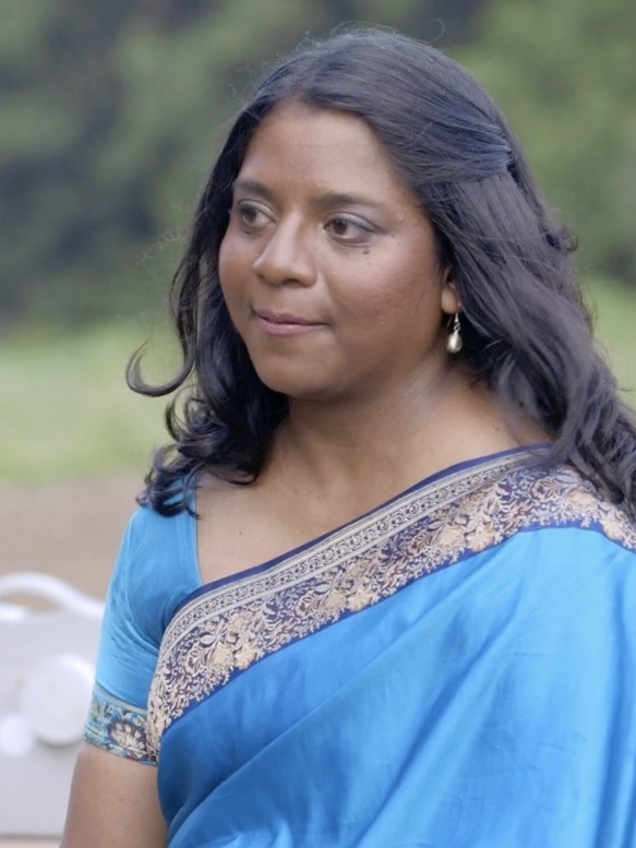 young woman in blue and gold saree sitting outside