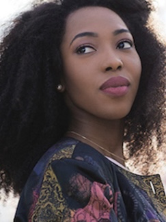 woman with pink lipstick and pink and blue shirt looking behind her shoulder