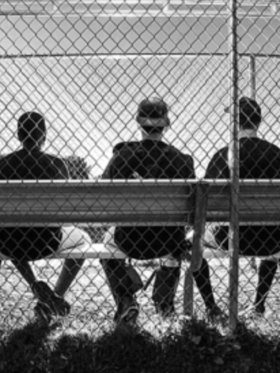 baseball players sitting on a bench against the park fence. black and white shot