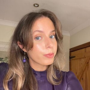 woman with brown hair and a purple shirt looking into the camera