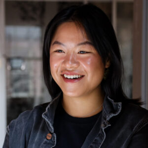 young woman with dark hair and a jean jacket smiling