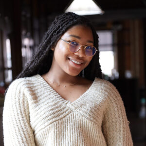 woman with white sweater and jeans and glasses standing in a halway