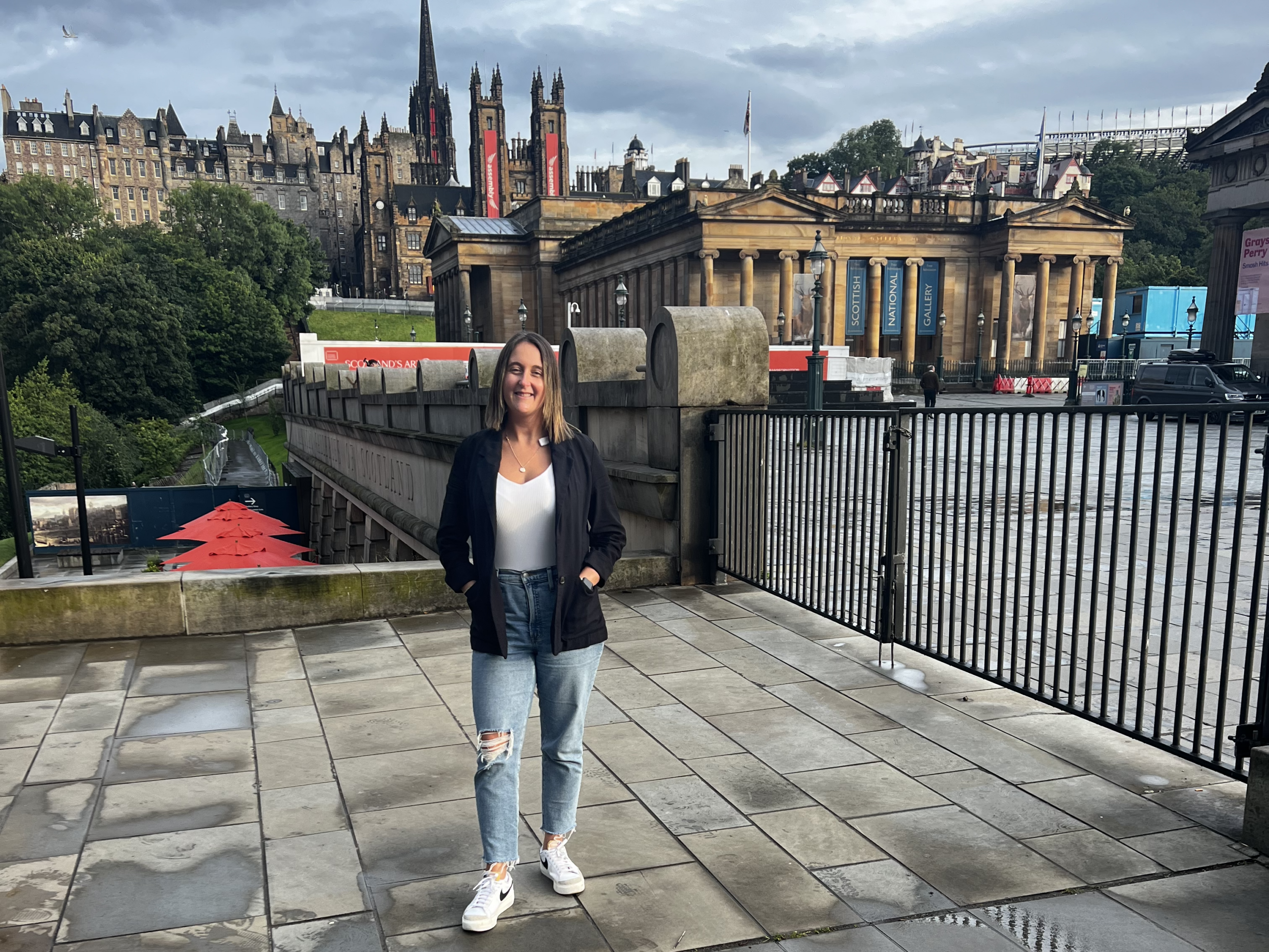 woman standing in Edinburgh with jeans and white sneakers.