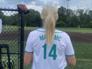 blonde woman with softball jersey on looking out at a field