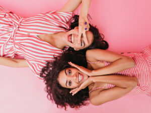 two women in pink smiling for a photo on a pink background