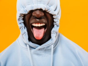 man in a blue hoodie with tongue out against a bright yellow background 