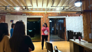 woman standing in brick office speaking in front of a crowd