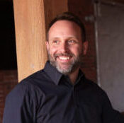 man standing in front of a wooden pole and a brick wall